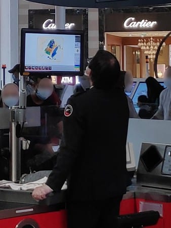 Agent de sécurité à un poste de contrôle d'aéroport regardant un écran de scanner de bagages, avec des passagers en arrière-plan